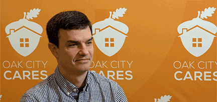 A photo of Corey with the Oak City Cares logos in the background