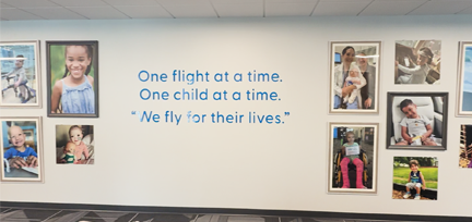 A wall with pictures of children and the words “One flight at a time. One child at a time. ‘We fly for our lives.’” 