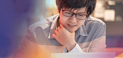 Photo of a man with glasses smiling while working on his laptop.