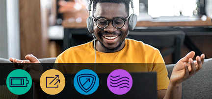 Photo of a man smiling while wearing headphones and using his laptop.